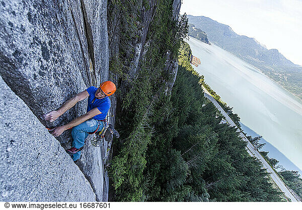 Mann klettert im Vorstieg auf Granit in Squamish mit Blick auf den Ozean im Hintergrund