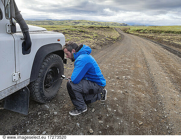 Mann kniend bei der Prüfung des Reifendrucks durch ein Gerät am Straßenrand