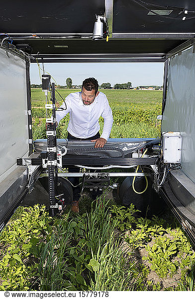 Mann kontrolliert Roboter  der Nutzpflanzen und Blumen auf landwirtschaftlichen Flächen in der Pixelfarming-Forschung überwacht