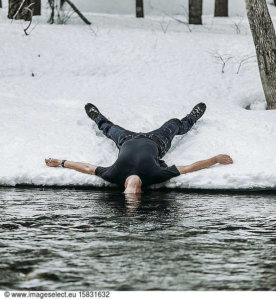 Mann liegt auf dem Rücken im Schnee ausgebreiteter Adler mit Kopf unter Wasser im Fluss