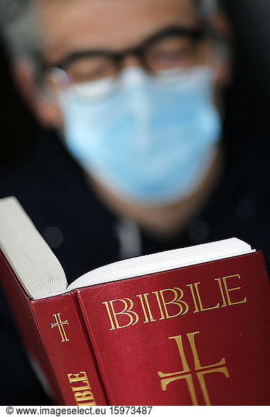 Mann liest die Bibel mit einer Einwegmaske  um das ansteckende Coronavirus zu vermeiden (COVID-19)  Frankreich  Europa