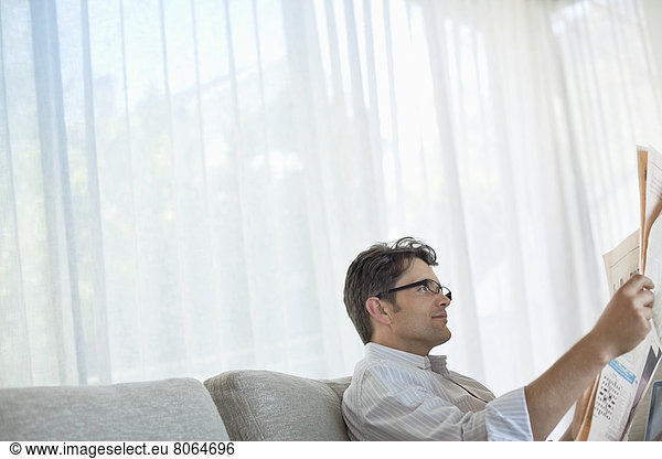 Mann liest Zeitung auf Sofa