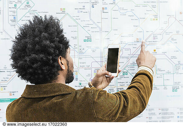 Mann mit Afrofrisur benutzt Smartphone beim Analysieren einer Karte