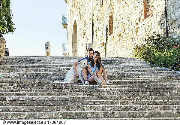 Mann mit Arm um Freundin sitzt mit Hund auf Stufen