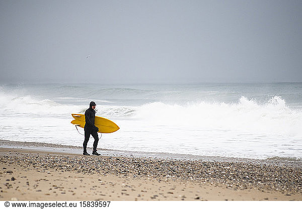 Mann mit gelbem Surfbrett am Winterstrand
