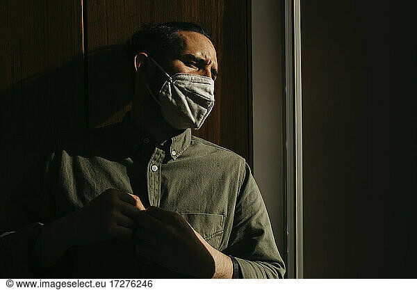 Mann mit Gesichtsschutzmaske beim Wegschauen zu Hause