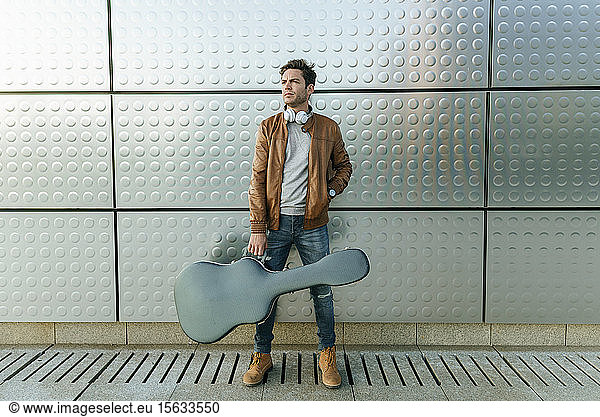 Mann mit Gitarre vor einer Silberwand stehend