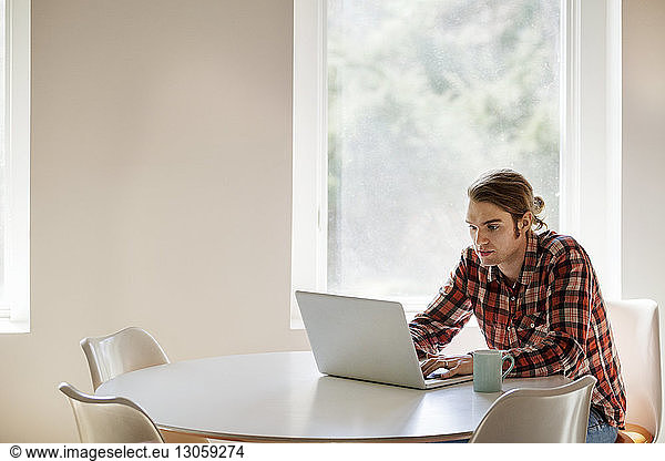 Mann mit Laptop am Tisch am Fenster