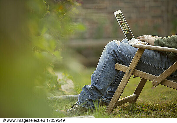 Mann mit Laptop im Liegestuhl im Garten