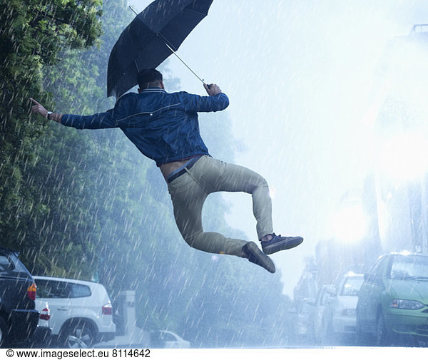 Mann mit Regenschirm springt im Regen