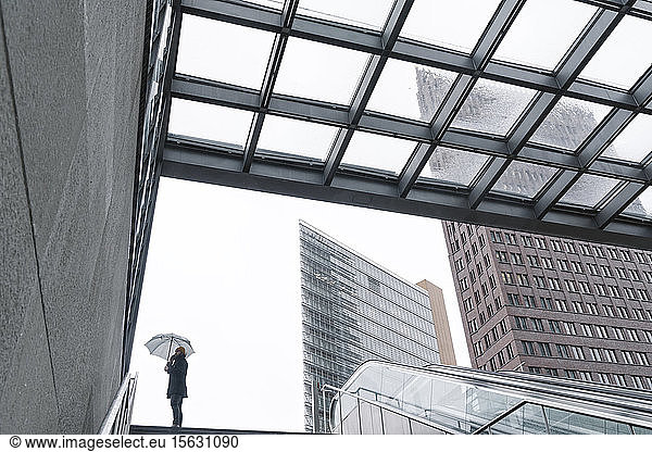 Mann mit Regenschirm telefoniert am Eingang des Bahnhofs Potsdamer Platz  Berlin  Deutschland