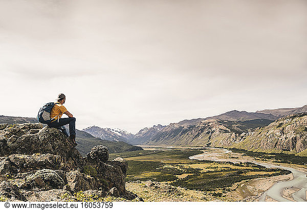 Mann mit Rucksack sitzt auf einem Felsen gegen den Himmel  Patagonien  Argentinien