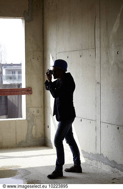 Mann mit Schutzhelm beim Fotografieren auf der Baustelle im Rohbau