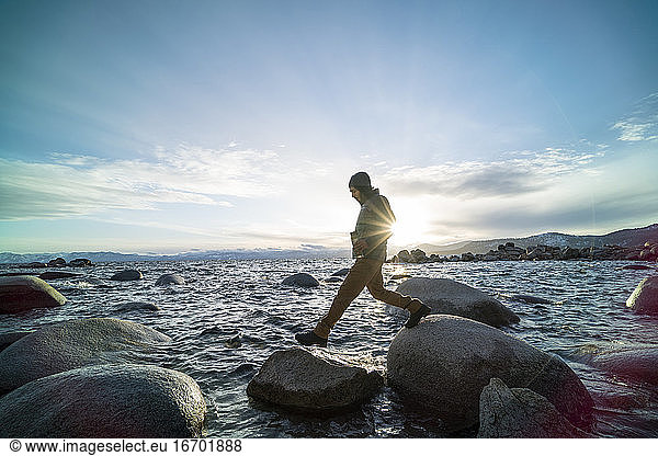 Mann mit Thermoskanne springt von Fels zu Fels über den Lake Tahoe
