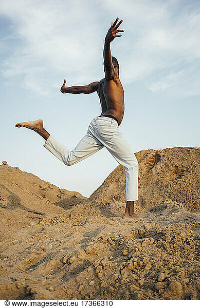 Mann ohne Hemd mit ausgestreckten Armen tanzt auf Sand