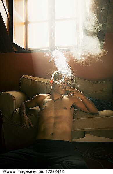 Mann ohne Hemd raucht im Wohnzimmer zu Hause
