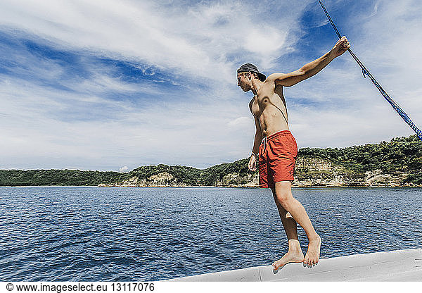 Mann ohne Hemd schaut aufs Meer  während er am sonnigen Tag im Boot vor bewölktem Himmel steht