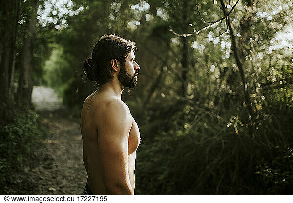 Mann ohne Hemd schaut im Wald weg