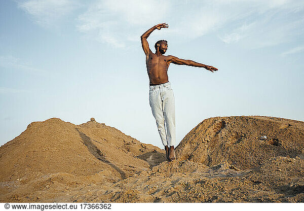 Mann ohne Hemd springt beim Tanzen auf Sand
