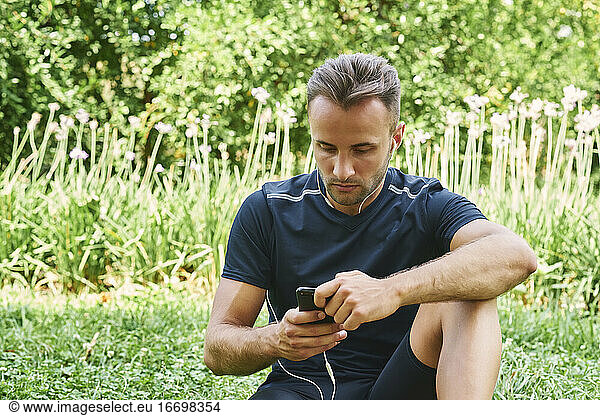 Mann ruht auf dem Gras in einem Park nach dem Training sitzen. Gesundes und gesundes Leben. Gesundheit und Sport Konzept.