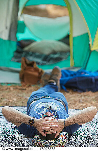 Mann ruht liegend vor seinem Zelt
