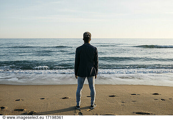 Mann schaut am Strand stehend auf die Aussicht