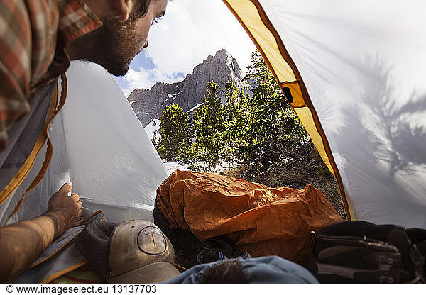 Mann schaut auf Berge  während er im Zelt sitzt