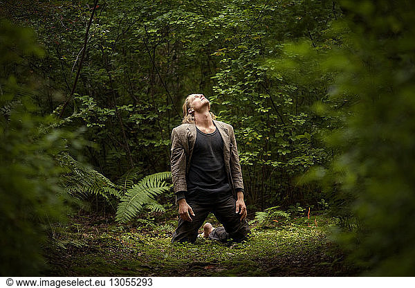 Mann schaut auf  während er auf einem Feld im Wald kniet