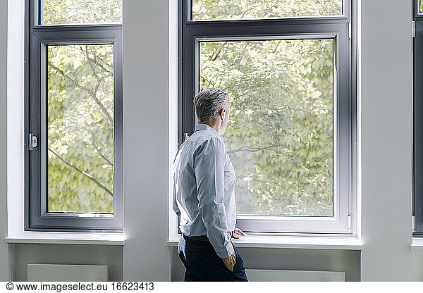 Mann schaut durch ein Fenster  während er im Büro steht