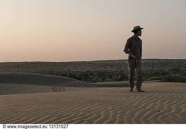 Mann schaut weg  während er bei Sonnenuntergang in der Thar-Wüste vor dem klaren Himmel steht
