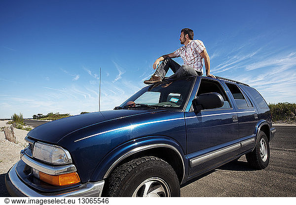 Mann schaut weg  während er im Auto vor blauem Himmel sitzt