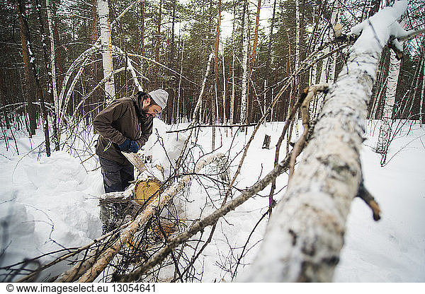 Mann schlägt Baumstamm in schneebedecktem Wald