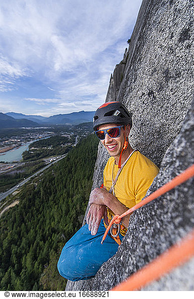 Mann sitzend in lustiger Position beim Klettern mit Helm und Sonnenbrille