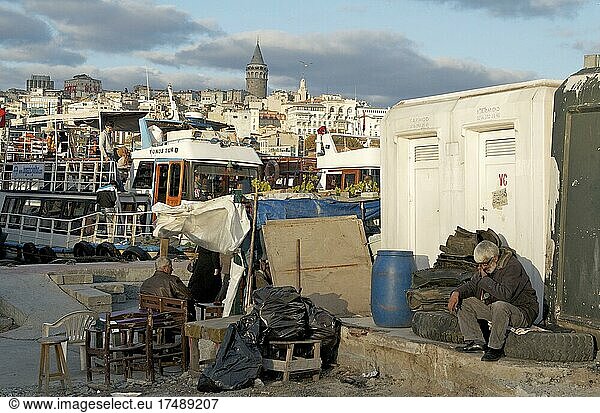 Mann sitzt auf alten Autoreifen im Hafenviertel von Eminönü mit Blick auf den Galata Turm  Istanbul  Türkei  Asien