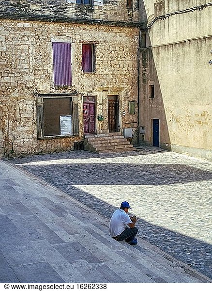 Mann sitzt auf den Stufen der Abbatiale Saint Gilles du Gard  Saint Gilles  Departement Gard  Provence  Frankreich.