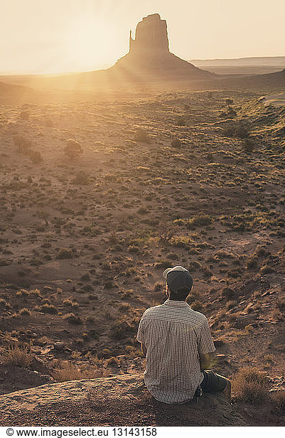 Mann sitzt auf einer Klippe und schaut bei Sonnenuntergang auf das Tal
