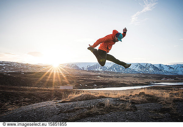 Mann springt mit Bergen und Sonne im Hintergrund