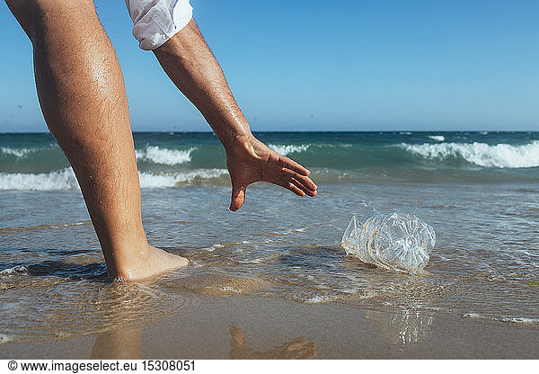 Mann steht am Meeresufer und hebt leere Plastikflasche auf