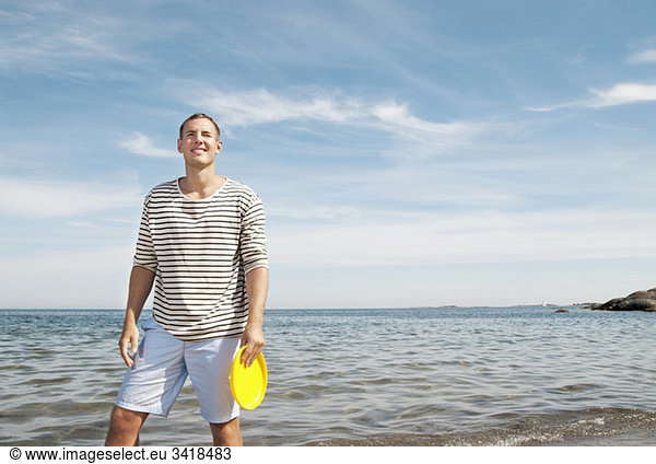 Mann steht am Strand und hält ein Frisbee.