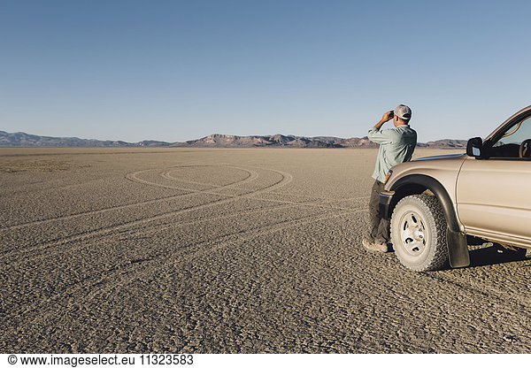 Mann steht auf riesiger Wüste  schaut durch ein Fernglas und lehnt sich an einen Lastwagen  Black Rock Desert