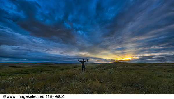 Mann steht mit ausgebreiteten Armen bei Tagesanbruch im Grasslands National Park; Saskatchewan  Kanada'.