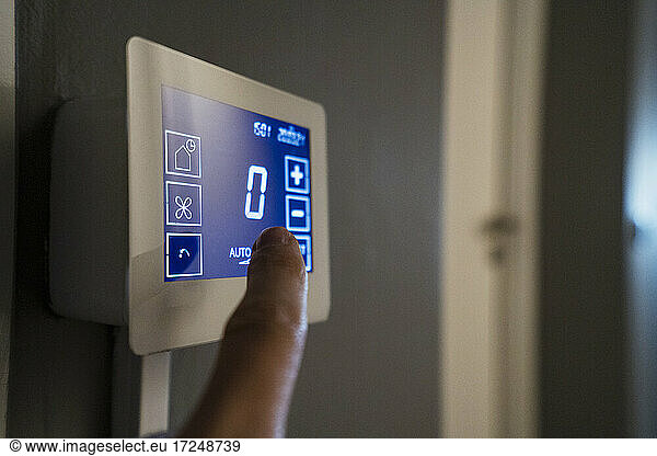 Mann stellt Temperatur am Thermostat über der Wand im Büro ein