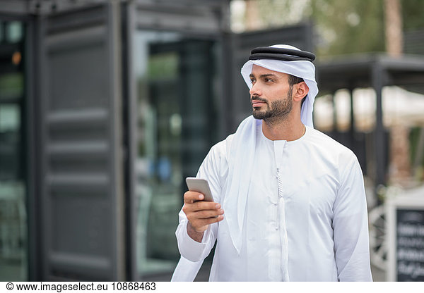 Mann trägt traditionelle Kleidung aus dem Nahen Osten mit Smartphone  Dubai  Vereinigte Arabische Emirate