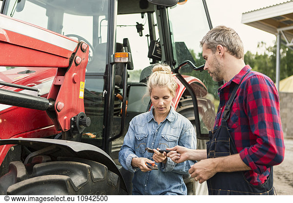 Mann und Frau halten Ausrüstung  während sie auf dem Bauernhof neben dem Traktor stehen.