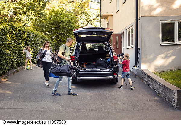 Mann und Frau laden Gepäck im Kofferraum  während der Junge das Elektroauto auflädt.