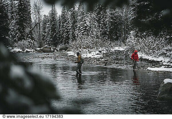 Mann und Frau spazieren im Fluss beim Fliegenfischen im Winter im Urlaub