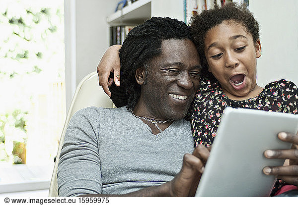 Mann und Tochter benutzen ein digitales Tablett und teilen sich den Bildschirm.
