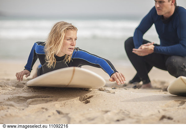 Mann unterrichtet Frau auf dem Surfbrett am Strand