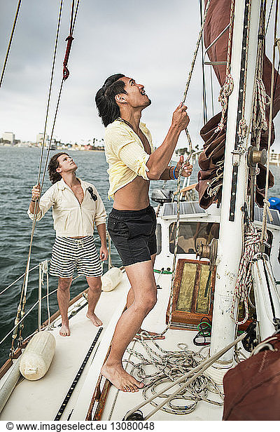 Mann verstellt Mast  während Freund im Segelboot reist