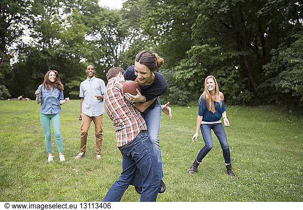 Mann verteidigt Frau mit Fussball in der Hand  während Freunde sie auf dem Feld beobachten
